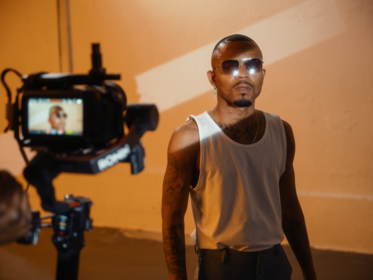 Young man with sunglasses posing for a cinematic shoot, showcasing modern street style and fashion.